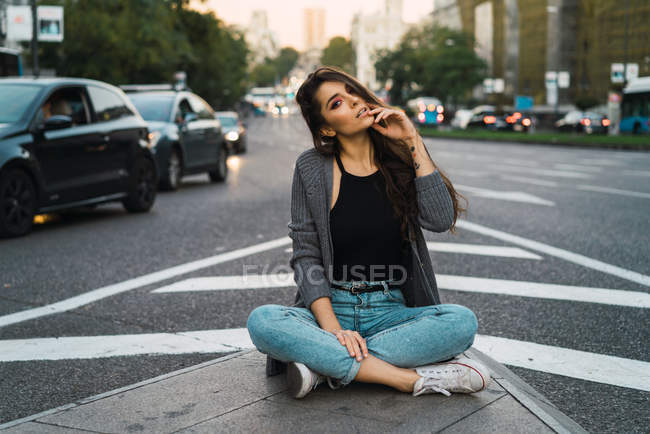 Jovem morena sentada na estrada de asfalto e olhando para a câmera . — Fotografia de Stock