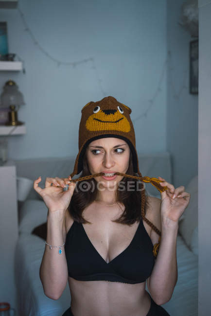 Brunette girl in black bra wearing knitted hat and biting tassel — Stock Photo