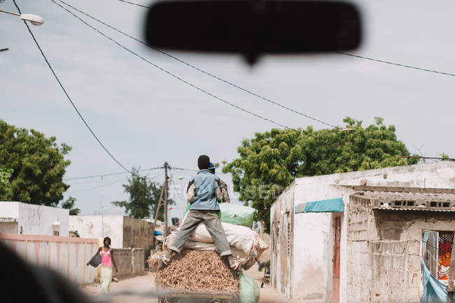 Goree, Senegal- December 6, 2017: View from car of child riding wagon on street of poor town. — Stock Photo