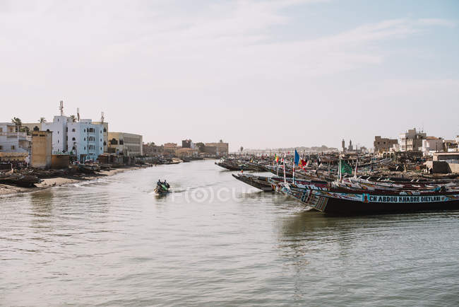 View boat sailing along moored boats on river of underdeveloped city in bright sunlight. — Stock Photo