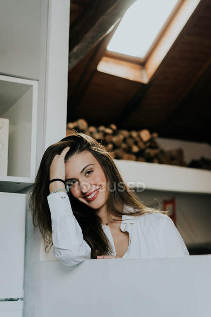 Morena joven sonriendo a la cámara y tocando el pelo - foto de stock