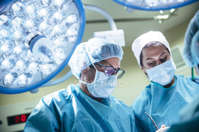 Retrato de médicos con máscaras mirando al paciente en la sala de cirugía - foto de stock