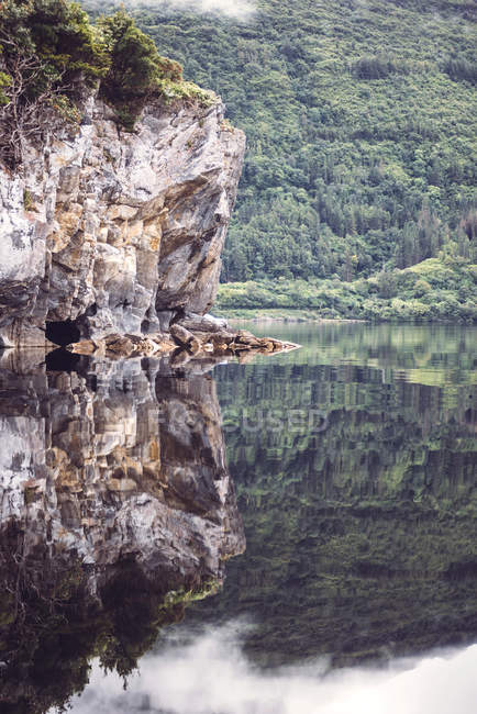 Acantilado rocoso que refleja la calma de la superficie del lago - foto de stock