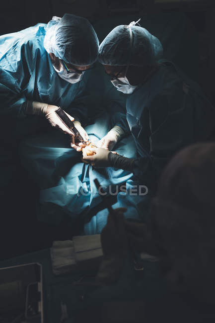 Grupo de cirujanos operando paciente bajo lámpara brillante - foto de stock