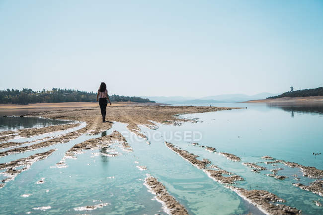 Жінка йде вздовж блакитного озера в сонячний день — стокове фото