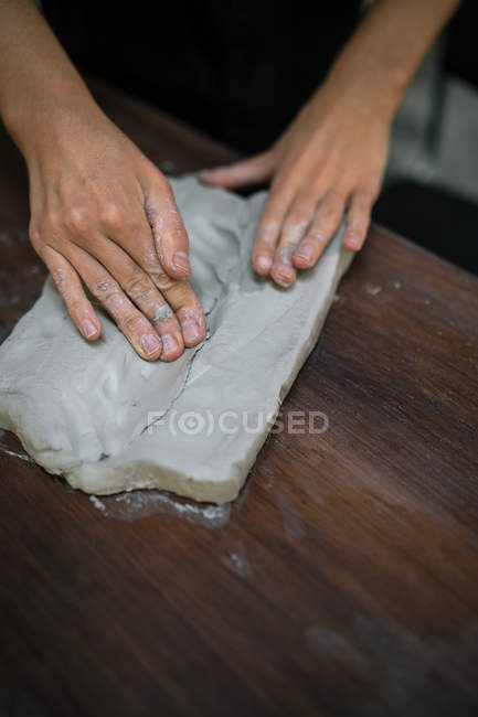 Cortar as mãos femininas amassar peça de argila na mesa de madeira — Fotografia de Stock