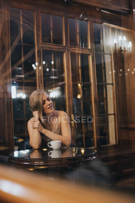 Vue de la fille blonde posant à la table du restaurant par la fenêtre — Photo de stock