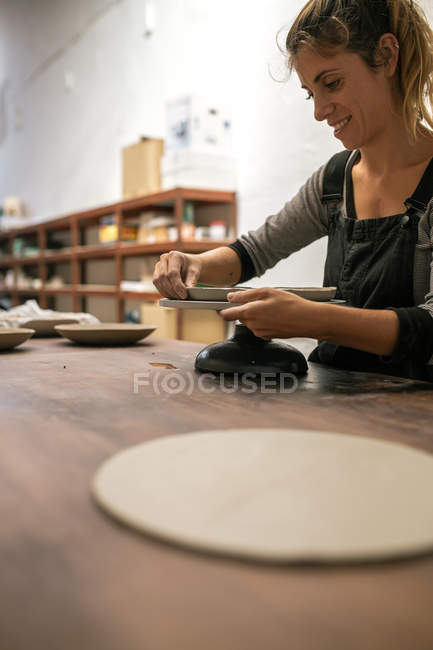 Vista laterale di donna bionda che forma il piatto con argilla a desktop — Foto stock