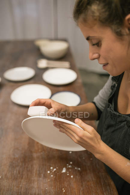 Konzentrierte Frau sitzt am Tisch und stellt Teller aus weißer Tonerde her. — Stockfoto