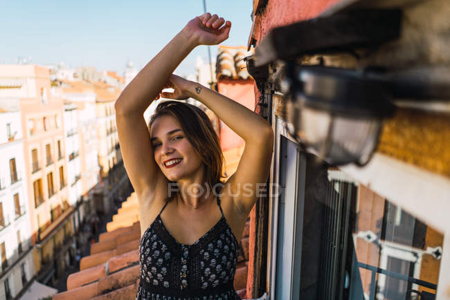 Porträt eines lächelnden brünetten Mädchens, das mit erhobenen Armen auf dem Balkon posiert — Stockfoto
