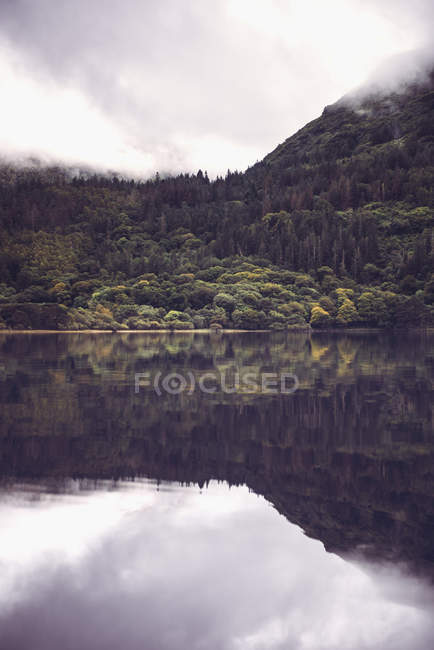 Reflection of misty green hill on calm water of lake — Stock Photo