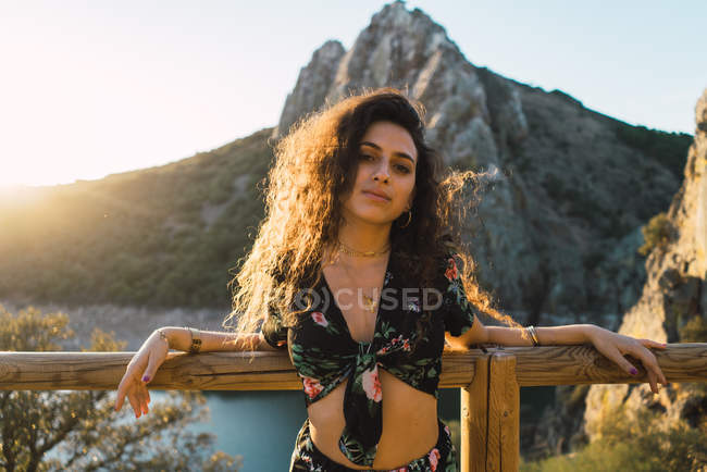 Portrait of brunette woman leaning on fence and looking at camera on mountain lake landscape background — Stock Photo
