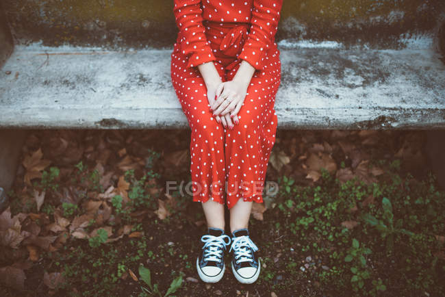 Crop female wearing red polka dots dress sitting on mossy stone bench — Stock Photo