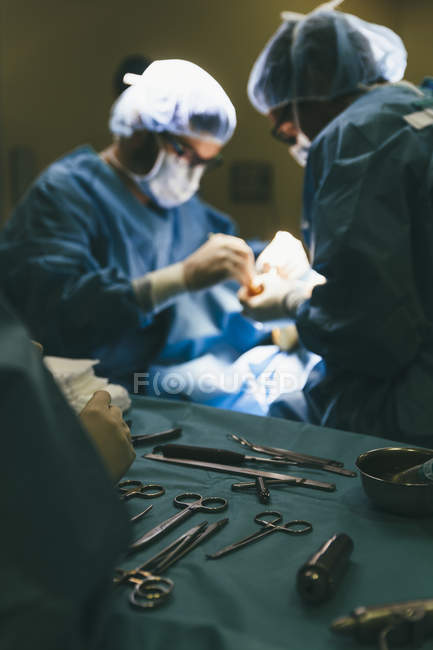 Vista de cerca de la mesa con instrumentos de cirugía en el fondo de los médicos que proporcionan la operación en el hospital - foto de stock