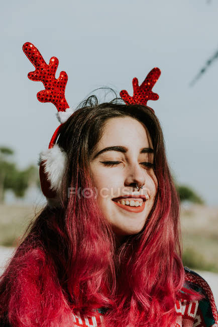 Lächelndes Mädchen mit Hirschhörnern Stirnband posiert mit geschlossenen Augen — Stockfoto