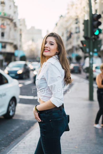 Seitenansicht einer brünetten Frau, die auf einem Fußgängerüberweg posiert und in die Kamera schaut — Stockfoto