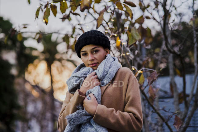 Portrait of young woman posing near tree with garland lights — Stock Photo