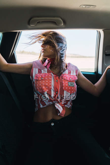 Retrato de menina morena inclinada para fora da janela do carro com o cabelo acenando no vento . — Fotografia de Stock