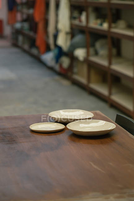 Trois assiettes artisanales brillantes sur table en bois à l'atelier — Photo de stock
