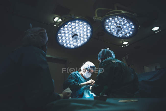 Grupo de cirujanos que operan pacientes bajo lámparas brillantes en el hospital - foto de stock