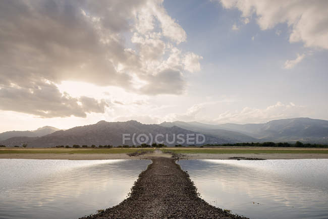 Symmetrical landscape with road amid of lake on beautiful summer sunset — Stock Photo