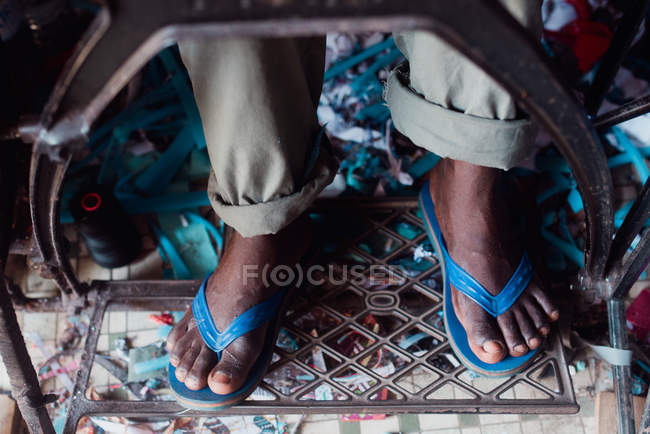 Unterteil einer Person in Flip-Flops, die Füße auf dem Pedal einer alten Nähmaschine hält. — Stockfoto