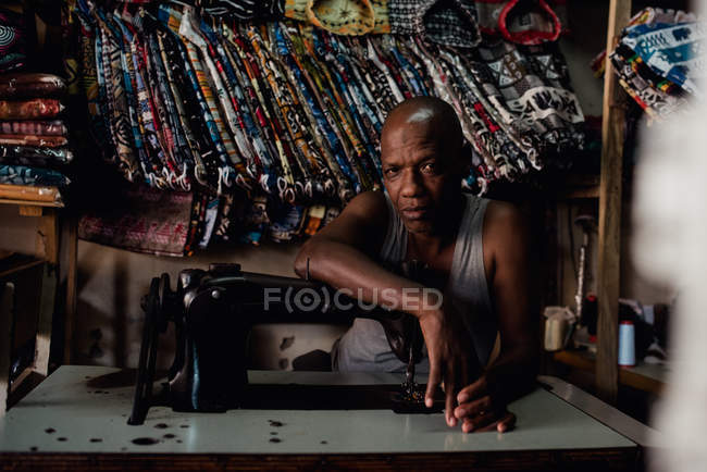 Goree, Senegal- December 6, 2017: Portrait of man leaning on old sewing machine at workshop and looking at camera. — Stock Photo
