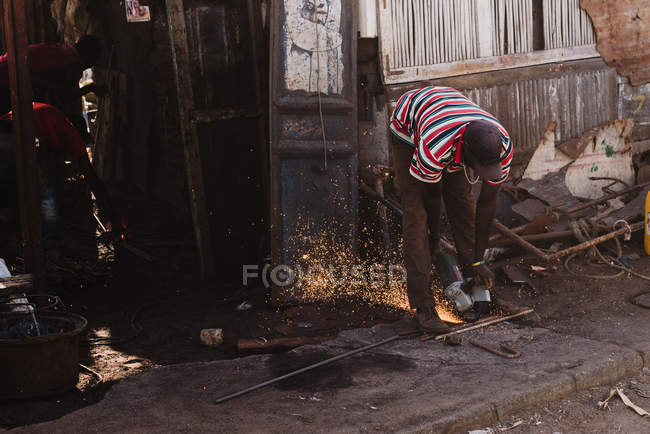 Черный мужчина-металлист распиливает кусок металла, работающий на улице, Гори, Сенегал — стоковое фото