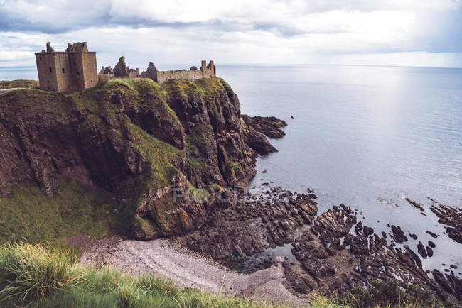 Distant view of Dunnottar Castle standing on cliff on seashore, Scotland. — Stock Photo