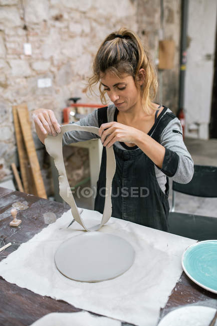 Женщина снимает глиняные обрезки с рабочего стола в мастерской — стоковое фото