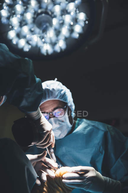 High angle view of surgeons operating patient in lamp light in hospital — Stock Photo