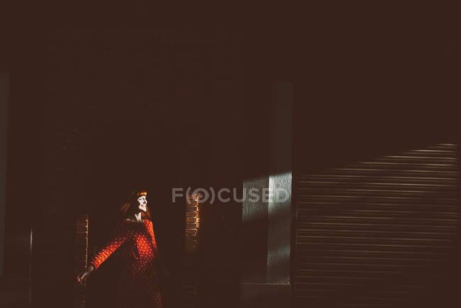 Fille gaie portant tenue rouge vif posant dans le rayon de soleil à côté du mur de briques . — Photo de stock