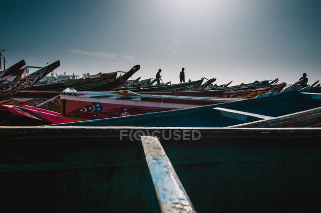 Yoff, Senegal- 6 de diciembre de 2017: Siluetas de niños caminando y jugando en barcos viejos en la orilla . - foto de stock