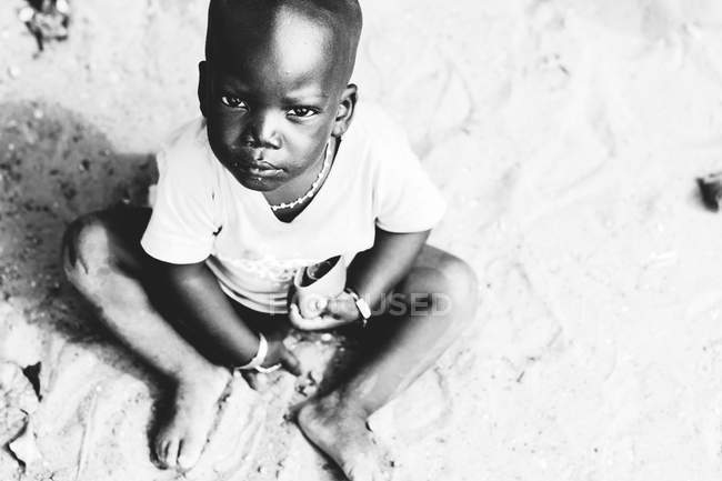 Yoff, Senegal- December 6, 2017: Low angle portrait of boy sitting on sand and looking at camera — Stock Photo