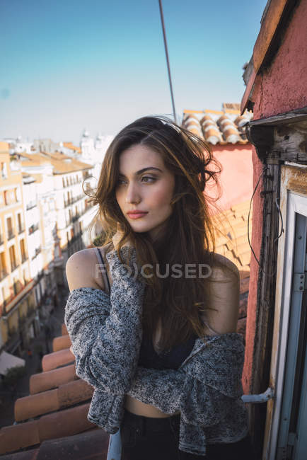 Confident brunette girl posing on balcony and looking aside with hand in hair — Stock Photo