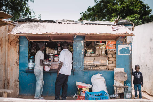 Yoff, Senegal- December 6, 2017: Exterior shot of street market stand with people doing purchases in sunlight. — Stock Photo