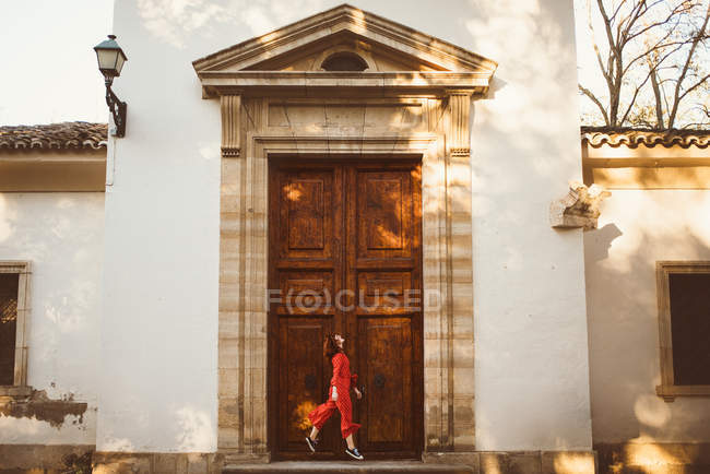 Vue latérale de la femme rousse sautant heureusement à la porte du vieil immeuble . — Photo de stock