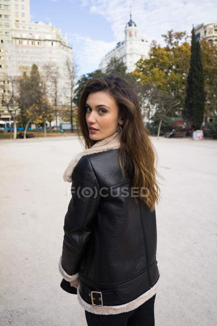 Brunette young woman walking at park alley and looking over shoulder at camera — Stock Photo