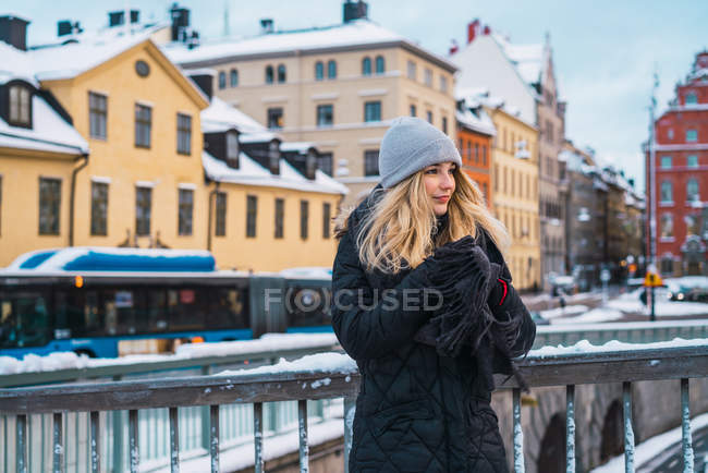 Вид сбоку блондинки, греющей руки на мосту в зимнем городе — стоковое фото