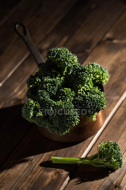 Still life of fresh bimi broccolis in rural copper sauce pot on wooden table — Stock Photo