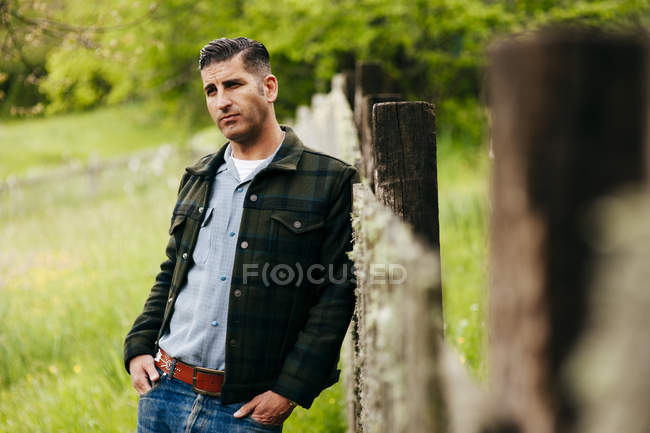 Retrato del hombre posando en el campo y apoyándose en la valla - foto de stock