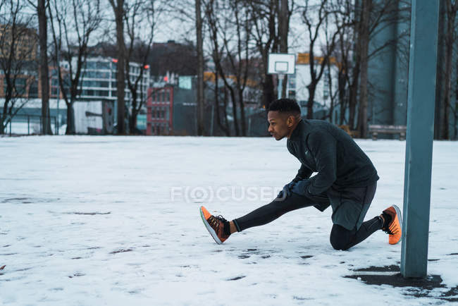Vista laterale dell'uomo atletico che riscalda i muscoli a terra al parco giochi — Foto stock