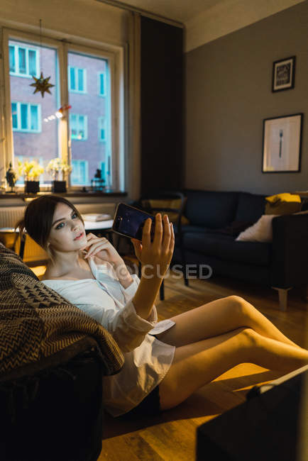 Портрет девушки на полу дома и селфи на смартфоне — стоковое фото