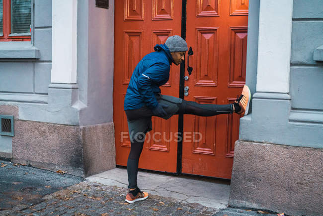 Seitenansicht eines Joggers, der sich mit dem Bein an die Wand lehnt und Muskeln aufwärmt und dehnt — Stockfoto