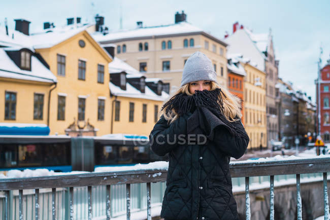 Portrait of young woman in warm clothes warming hands while standing on winter street. — Stock Photo