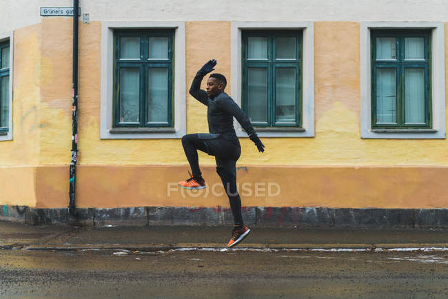 Вид збоку бігуна в теплому одязі, що стрибає через асфальт — стокове фото