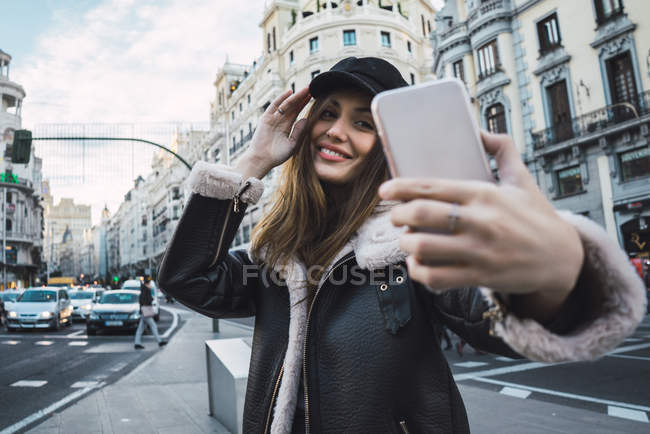 Portrait of woman touching cap and taking selfie on street — Stock Photo