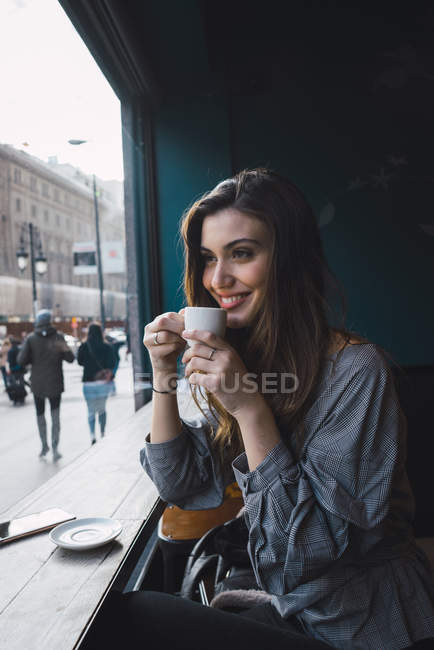 Портрет улыбающейся брюнетки, пьющей кофе в кафе и отворачивающейся — стоковое фото