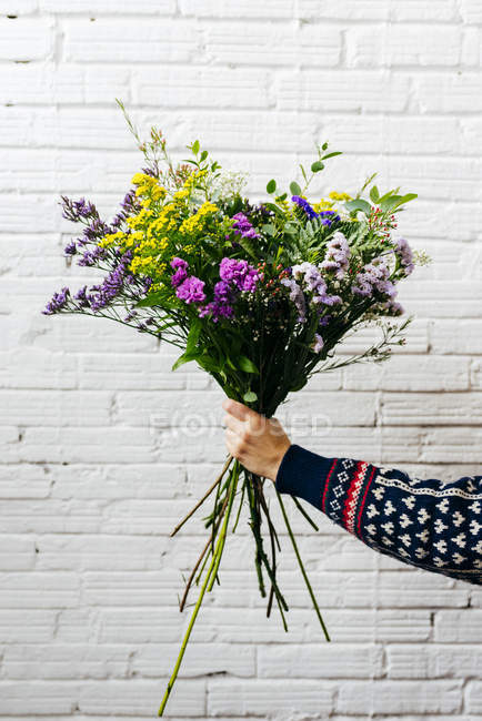 Crop hand holding elegant flower bouquet on background of white brick wall. — Stock Photo