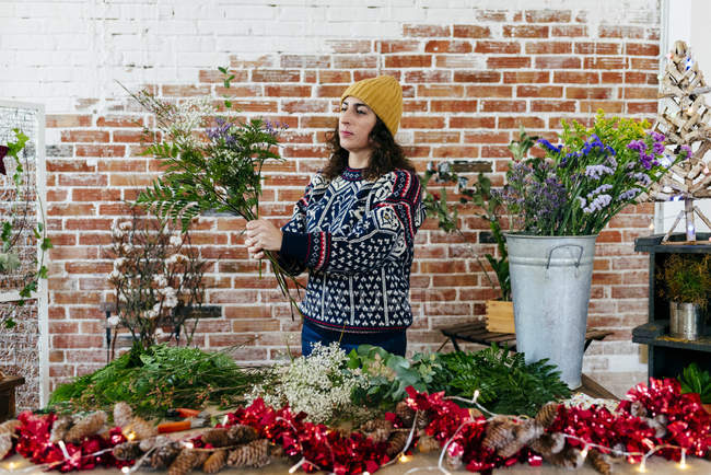 Portrait of woman in knitted sweater and hat arranging flower bouquet over brick wall on background — Stock Photo
